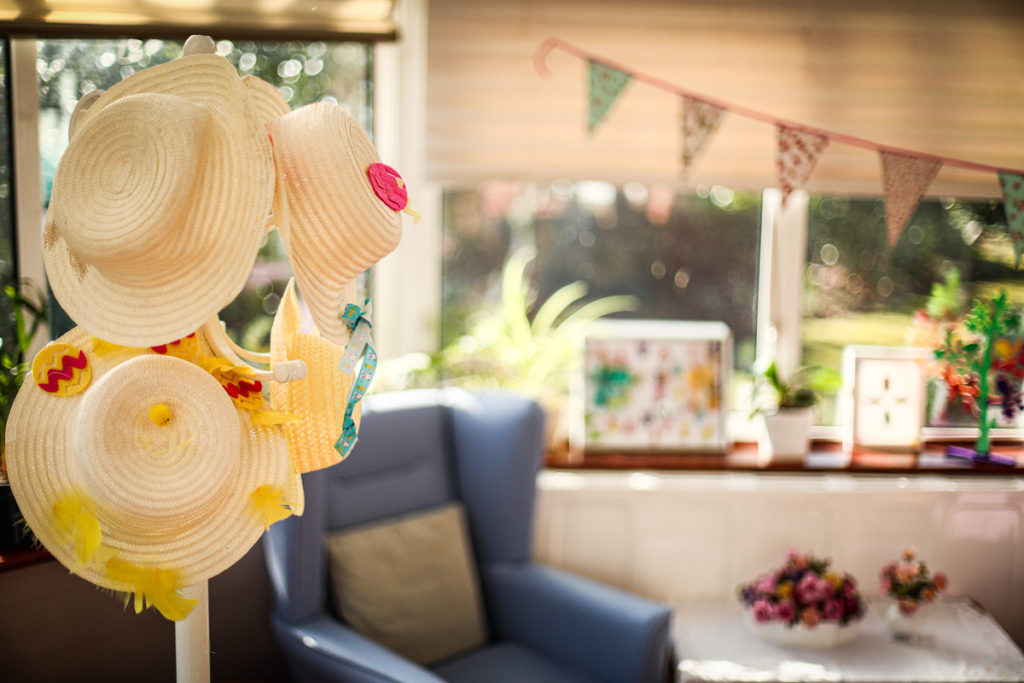 hats hanging in front of a blue chair beside a window at a care home