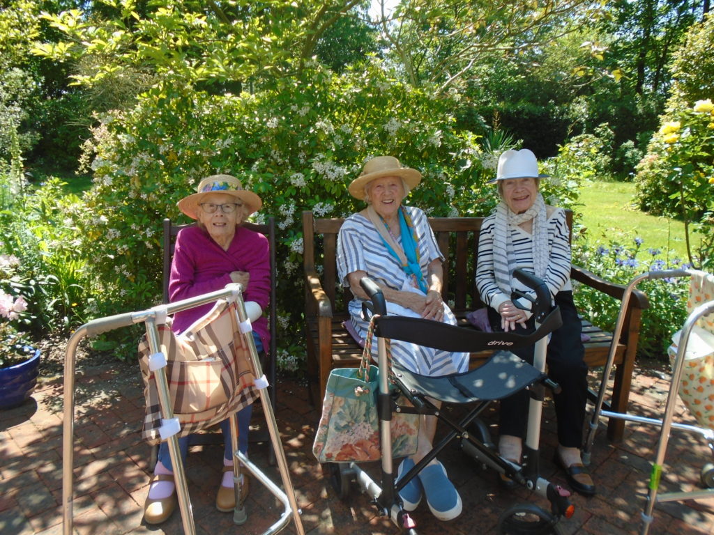 our care home residents sitting on a bench beside a green hedge